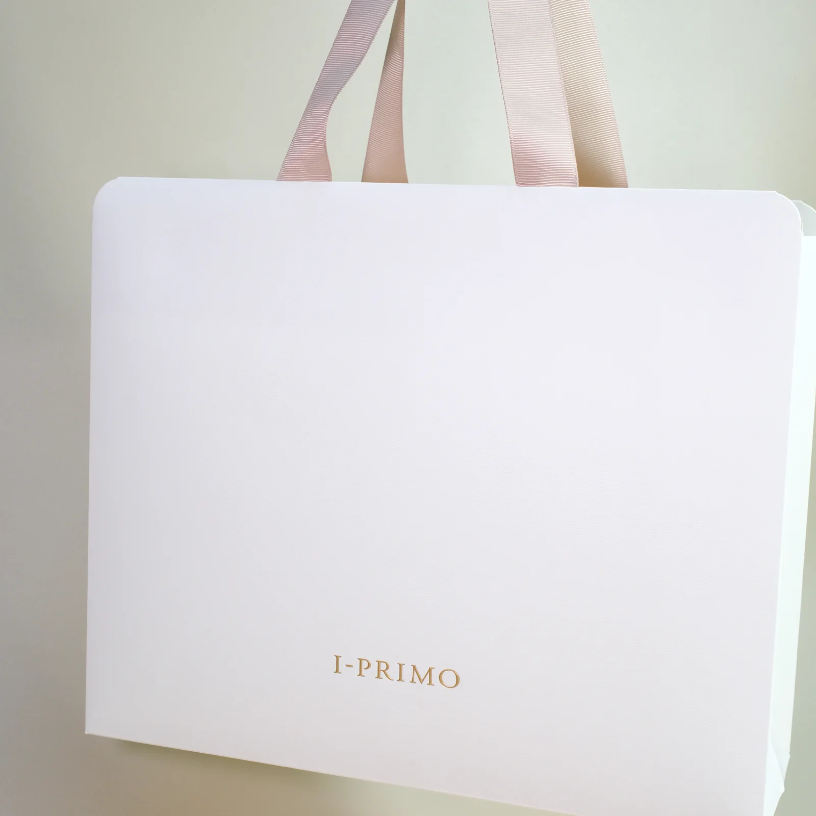 白色 I-PRIMO 紙袋,袋口圓角,粉色絲帶手挽,正面下方細小燙金 Logo